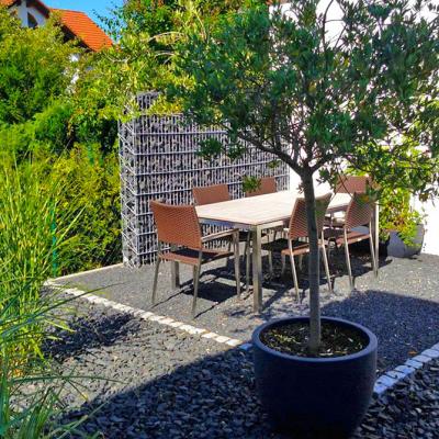 Ein bepflanzter Steingarten mit kleiner hervorgehobener Terrasse mit Gartenmöbel.